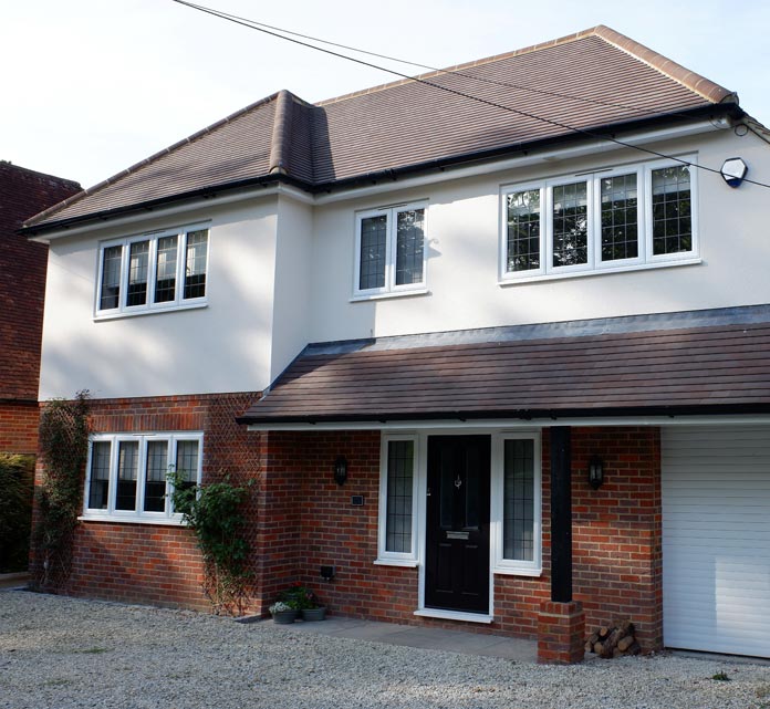 A two-story suburban house with a red brick lower facade and pale cream upper walls topped by a brown tiled hipped roof. The front features white-framed multi-pane windows, a small porch with a matching tiled roof.