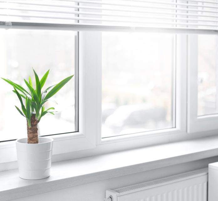 A bright, minimal interior with a wide window with partially raised horizontal blinds lets in soft, diffused daylight, creating a clean, airy, and modern atmosphere.