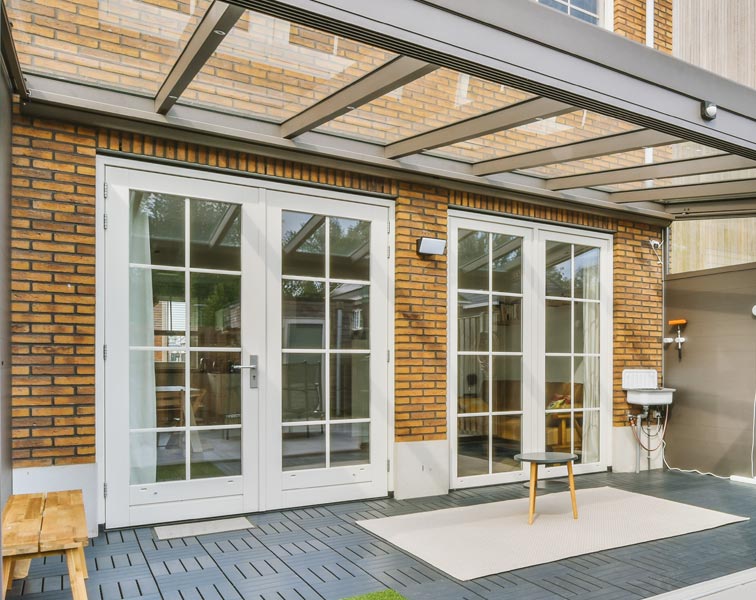 A covered patio attached to a brick house with two sets of white-framed French doors.